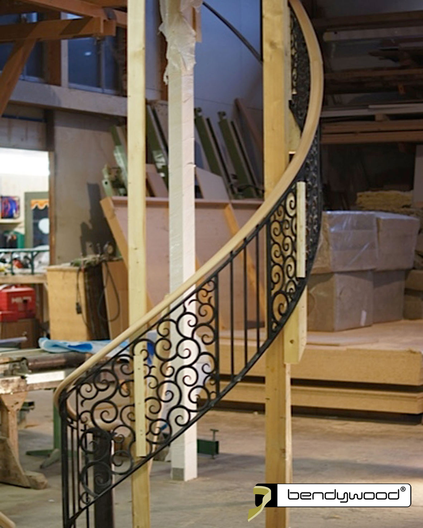 Pasamanos ovalados en haya Bendywood® para una escalera curvada con barandilla de hierro forjado.